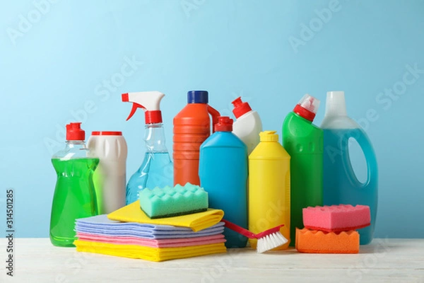 Fototapeta Bottles with detergent and cleaning supplies on blue background, space for text