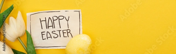 Fototapeta top view of Easter egg, tulips and greeting card with happy Easter lettering on yellow colorful background, panoramic shot
