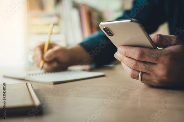 Fototapeta hand holding using texting cell phone and typing computer.businessman at workplace Thinking investment plan.chatting contact Investor.searching for information use internet.connecting people concept