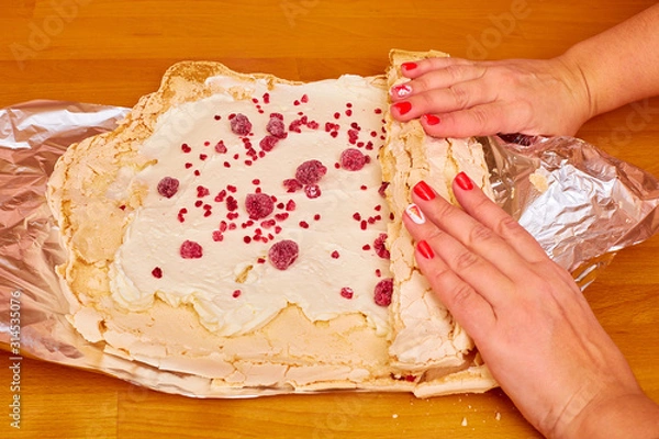 Obraz women's manicured hands wrap a roll with cream cream with raspberries on a shiny foil