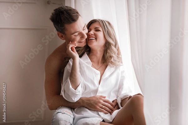 Fototapeta loving couple having fun together at home, playful wife biting smiling husband ear, piggyback, man and woman playing childish in bed, enjoying funny intimate moments