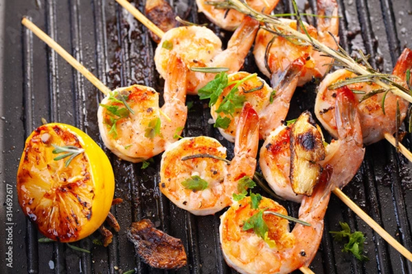 Fototapeta grilled shrimp on skewers. Grilled seafood on skewers with spices, herbs and lemon. delicious prawn. Grill. The iron grill. close up