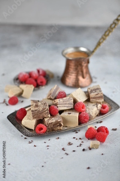 Fototapeta Oriental sweets, halva slices on a metal dish, decorated with raspberries, with Turkish coffee. Background, vertical.