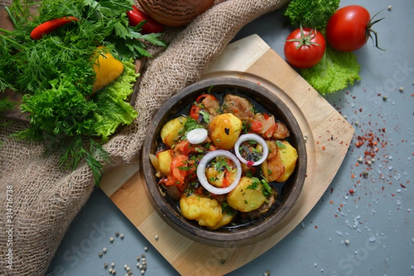 Fototapeta Beef, pork, lamb, meat and vegetables are stewed in a black bowl with fried potatoes. Dark background. Copy space. View from above.
