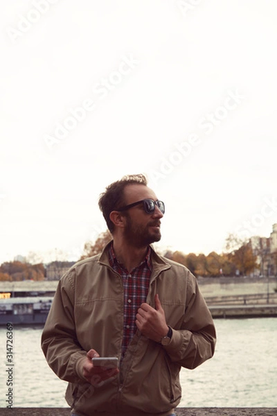 Fototapeta Handsome man using cellphone while enjoying in Paris.