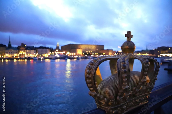 Fototapeta Gilded Crown on Skeppsholmsbron by dusk with dramatic dark collored sky at the river with a view at Gamla Stan in Stockholm Sweden. Focus is on the Crown.