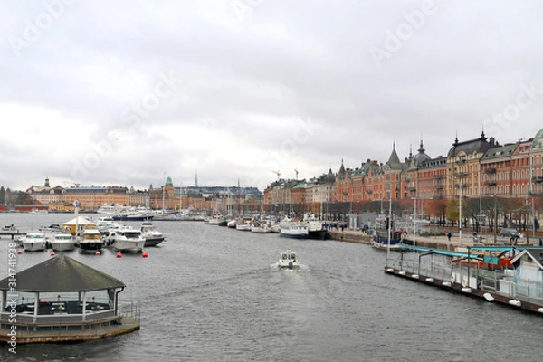 Fototapeta Harbor of stockholm in sweden. To the riverside with houses in red and yellow collors. Boats on the river on a fall dat with overcast