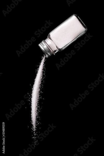 Obraz Salt is poured from a salt shaker on a black background. Salt shaker spills salt. A stream of salt.