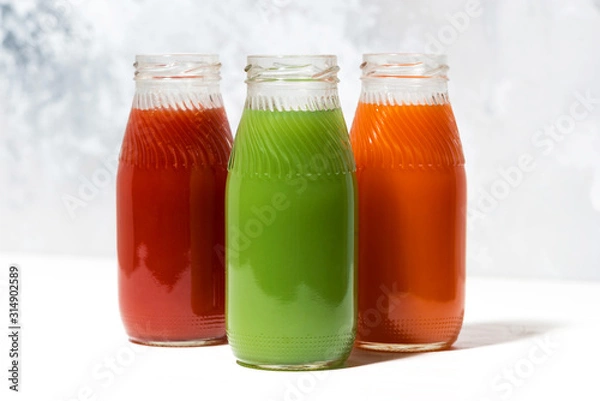 Fototapeta colorful vegetable juices in bottles on white table, closeup