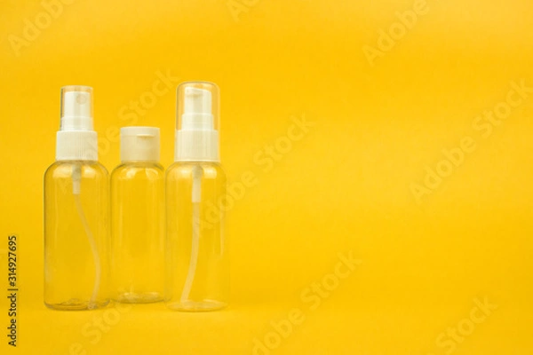 Fototapeta Empty cosmetic plastic bottles with pump and spray on yellow background with copy space. Clear cosmetic containers kit for travel. Template, mockup for advertising, web, social media. Stock photo.