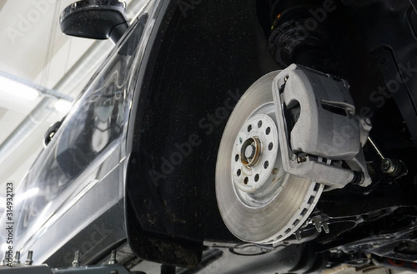 Fototapeta The front brake disc and brake caliper are mounted on a modern car. Design and elements. Original spare parts and quality service and repair.
