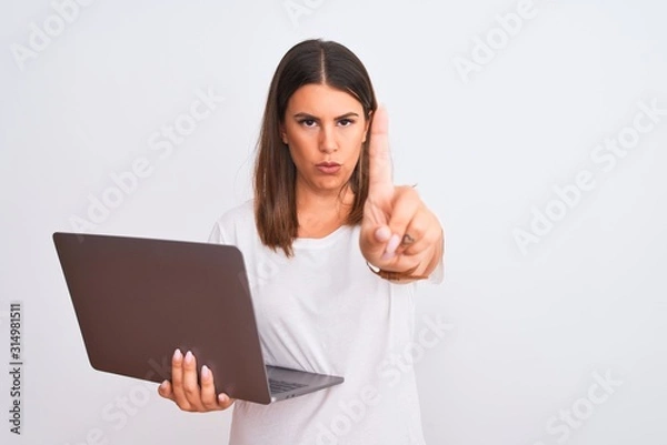 Obraz Beautiful young woman working using computer laptop over white background Pointing with finger up and angry expression, showing no gesture