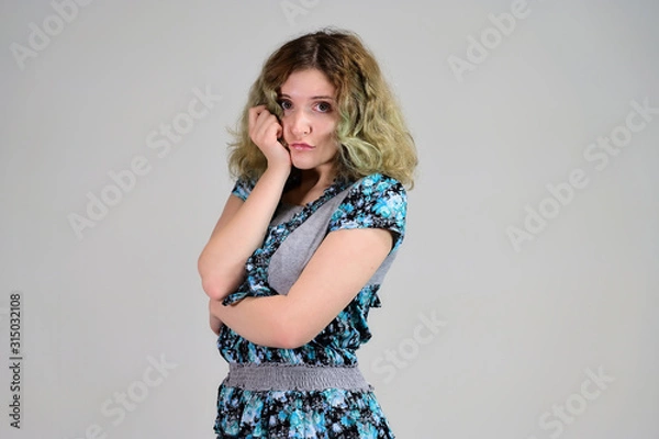 Fototapeta Concept horizontal photo of a young woman with emotions in a turquoise dress stands in front of the camera on a white background. Portrait of a student girl with beautiful magnificent hair.