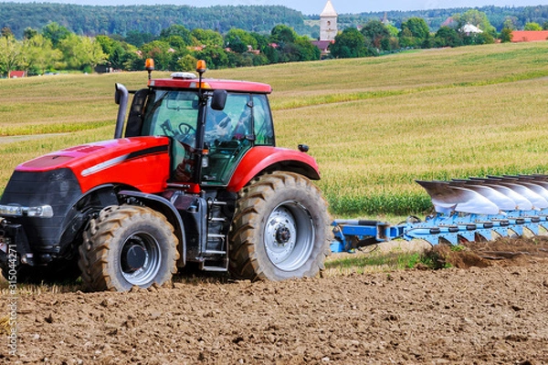 Fototapeta Farmer in red tractor preparing land with plow for sowing