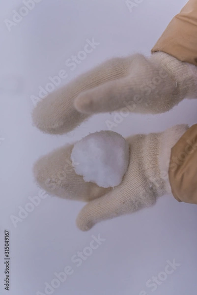 Fototapeta Woman makes a snowball in the hands of white mittens