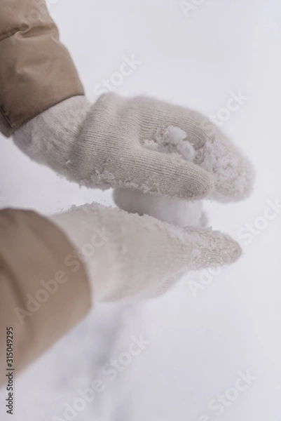 Fototapeta Woman makes a snowball in the hands of white mittens