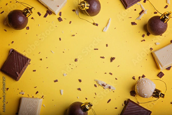 Fototapeta Christmas New Year balls made of chocolate and pieces of white and dark chocolate on a bright yellow background. View from above. Flat lay.