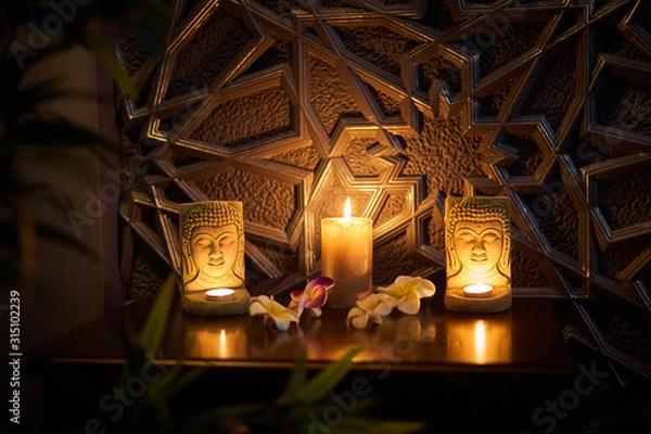 Fototapeta There is a candle on the table, on the sides of the candle are two statuettes of the Buddha, behind the candles is a golden tree. Thai style