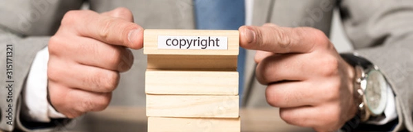Fototapeta cropped view of businessman holding wooden block with copyright inscription isolated on grey