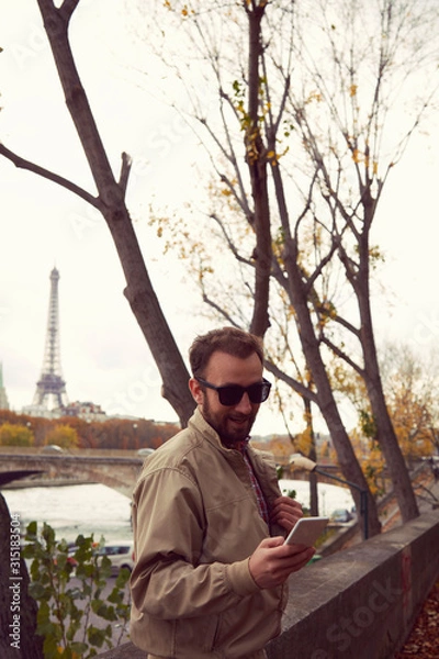 Fototapeta Handsome man using cellphone while enjoying in Paris.
