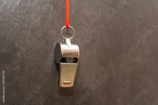 Fototapeta silberne Trillerpfeife hängt vor einer grauen Wand