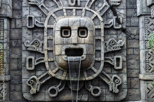 Fototapeta Waterfall in a stone wall and a sculpture of ancient Mayans with dragons and snakes