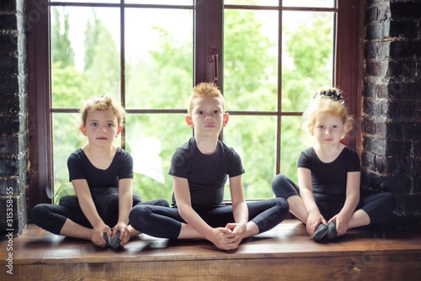 Obraz Portrait of 3 little children dancer two girls and one boy in black leotard sitting on window at dance studio. Recovery on dancing lesson. Kids hobby dancing. Active lifestyle in childhood