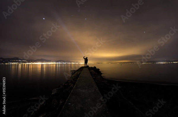 Fototapeta lonely man in perspective, at night, facing the lake, reflections, flashlight, isolated