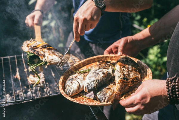 Fototapeta Mężczyzna trzyma talerz z gotowym posiłkiem. pyszna i świeża ryba z grilla z cytryną na grillu w ogrodzie w okresie letnim. Makro selektywnej ostrości strzał z płytkiej głębi ostrości