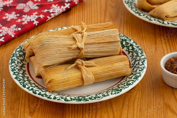 Fototapeta Pork Tamales on a white and green plate on a pine table with a red napkin and salsa