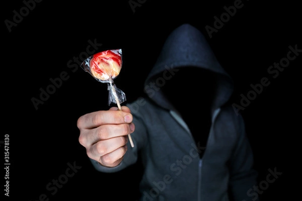 Fototapeta Unknown man holds out candy on a stick.