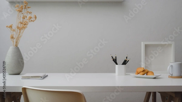 Fototapeta Close up view of workspace with copy space, decorations, stationery, coffee cup and croissant on white table with white wall