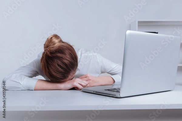 Fototapeta Overworked and tired sleeping over a laptop in a desk at work in her office