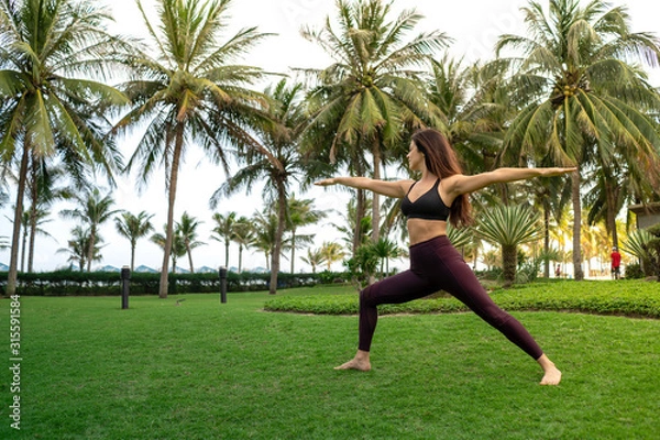 Obraz  A girl practicing yoga on a beautiful tropical grass field surrounded by palm trees
