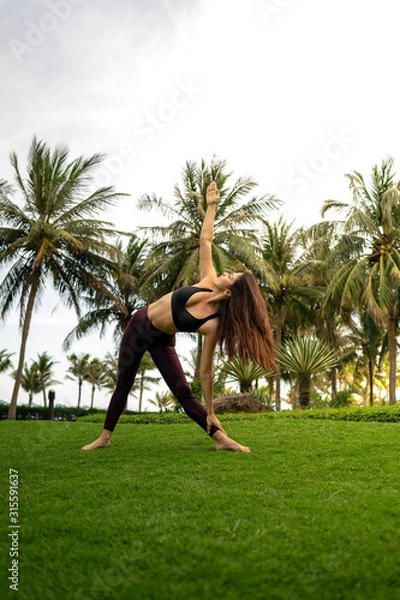 Obraz  A girl practicing yoga on a beautiful tropical grass field surrounded by palm trees