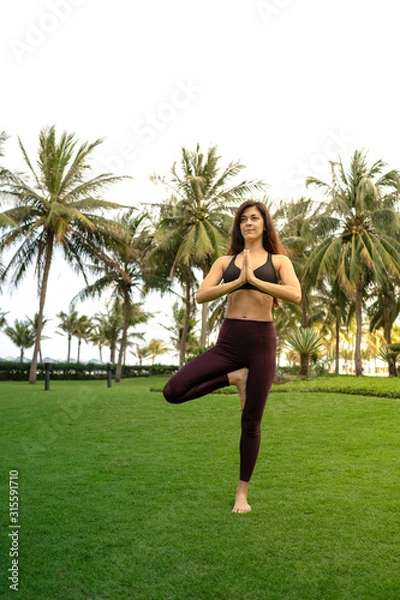 Obraz  A girl practicing yoga on a beautiful tropical grass field surrounded by palm trees