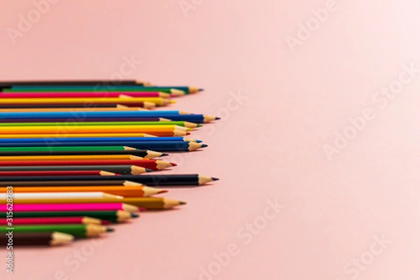 Fototapeta Colored pencils of different lengths are scattered, extending into the distance, on a pink background on the left side, tending to the center. Horizontal side view