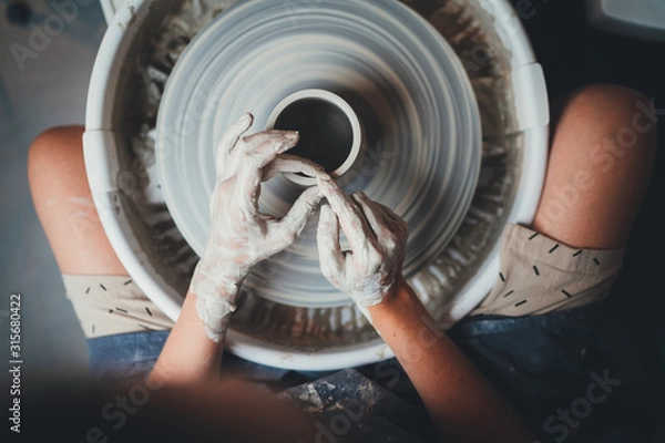 Obraz Top view of female potter's hands working on pottery wheels with eco friendly clay makes mug, concept for workshop and master class, Handcraft Ceramic Art People 
