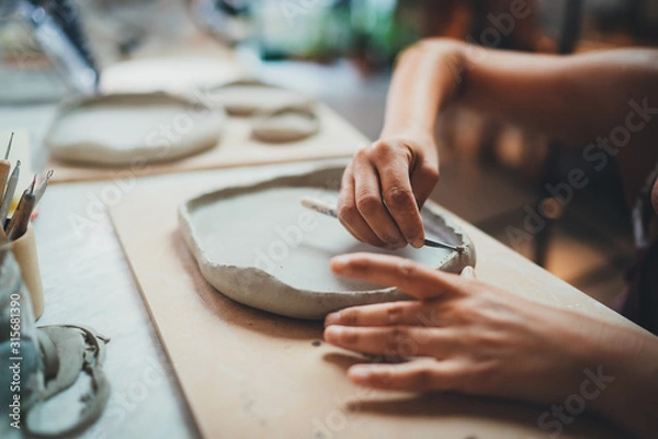 Obraz Zbliżenie kobiecych rąk współpracujących z gliną sprawia, że ​​przyszła płyta ceramiczna, profesjonalny artysta ceramiczny wykonuje zajęcia z ręcznego budowania w warsztacie nowoczesnej ceramiki, kreatywny projekt rzemieślniczy