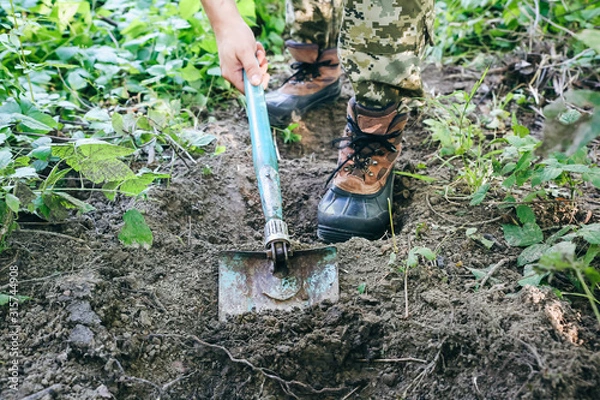 Obraz Man is digging ground with a shovel. Tourist in the nature. Making stairs outdoors.
