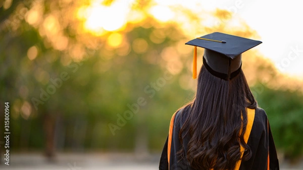 Obraz Female graduates wear black gowns and yellow tassels waiting to attend the commencement ceremony at the university.