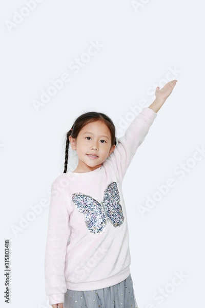 Obraz Little kid girl standing and points hand up present something on white background. Asian schoolgirl in education concept.
