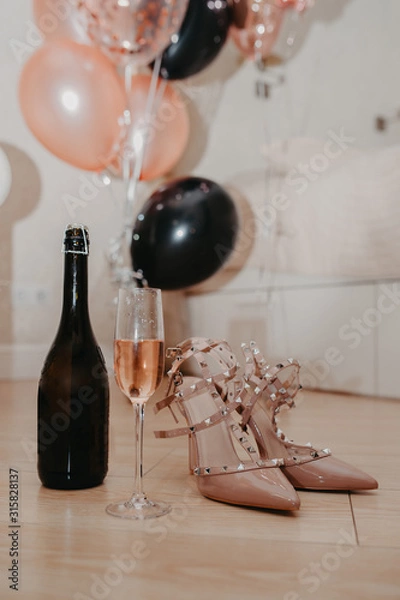 Fototapeta invitation card for a bachelorette party, stylish beige sandals with spikes, a glass of pink champagne and a bottle on a background of pink and black balloons horizontally