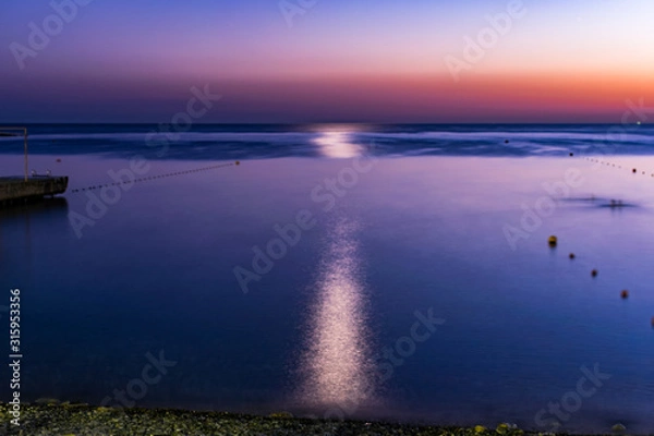 Fototapeta Красивый, красочный и контрастный закат над морем, океаном. Горячее солнце освещает просторный пейзаж, отбрасывая блики лучей на водную гладь. Яркий солнечный восход. Путешествие и туризм.