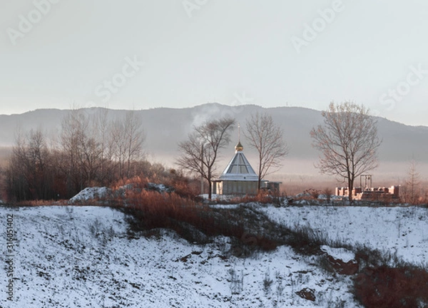 Fototapeta A small monastery building on a frosty winter morning on a background of hills covered with foggy haze