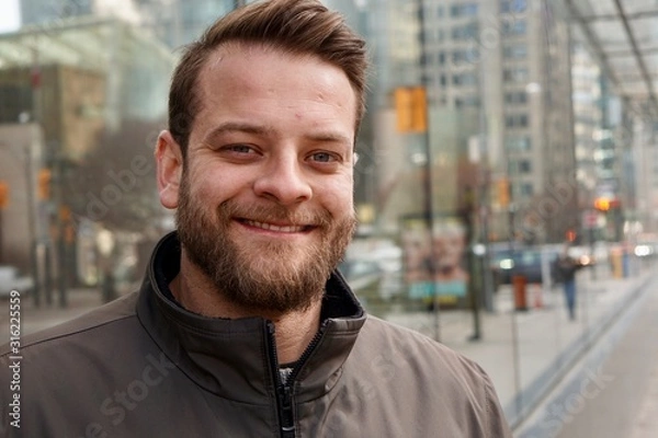 Fototapeta Man with a beard smiling in downtown Toronto with sky rise buildings in the background