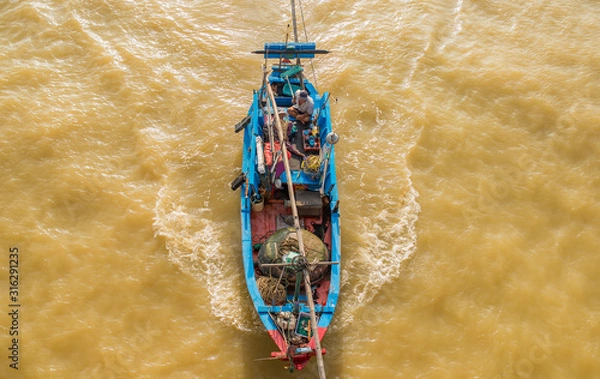 Obraz A small fishing wood boat is sailing in the sea for fishing. The photo was taken from above. Brown seawater due to the recent typhoon and many river sediment.