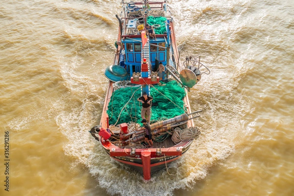 Obraz A large fishing boat with people on board sailing in the sea for fishing. The photo was taken from above. Brown seawater due to the recent typhoon and many river sediments.