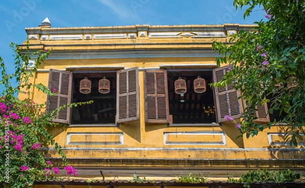 Obraz Typical view of Hoi An ancient town streets. The second floor of the cafe building. Open wooden shutters on the windows. Birdcages hang in the window opening.