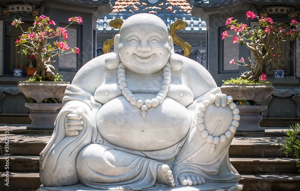 Obraz A statue of a seated and smiling Buddha in the territory of one of the Pagodas located in Hoi An city, Vietnam. The statue is made of white marble.